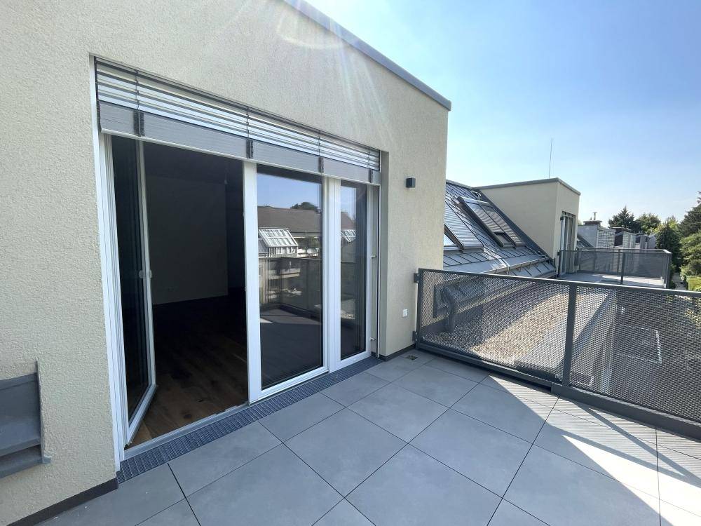Heller Balkon mit Fliesenboden und Zugang zu Innenräumen, umgeben von weiteren Gebäuden.