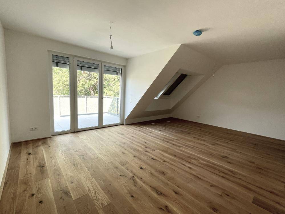 Helles Zimmer mit Holzboden, Dachschräge und Zugang zu einem Balkon, ideal für Wohnen oder Schlafen.