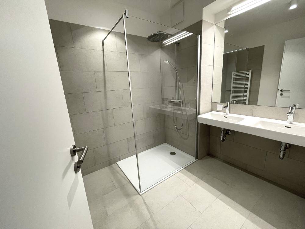 Modernes Badezimmer mit Doppelwaschbecken, großer begehbarer Dusche und hellen Fliesen.
