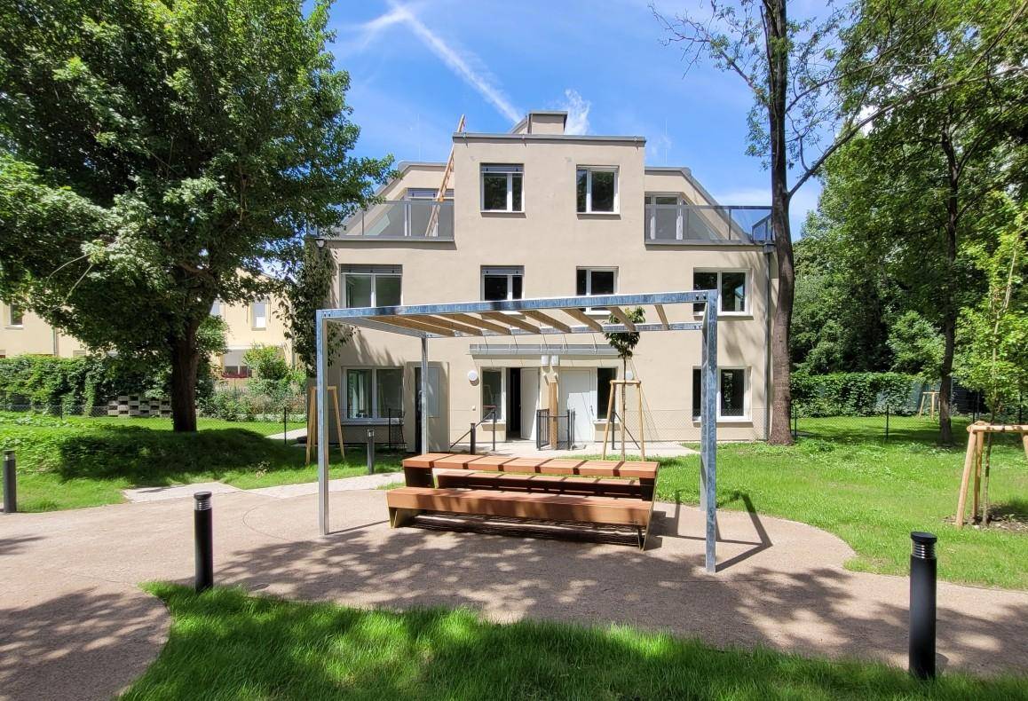 Modernes Wohngebäude umgeben von Bäumen und einer Pergola mit Sitzgelegenheiten.