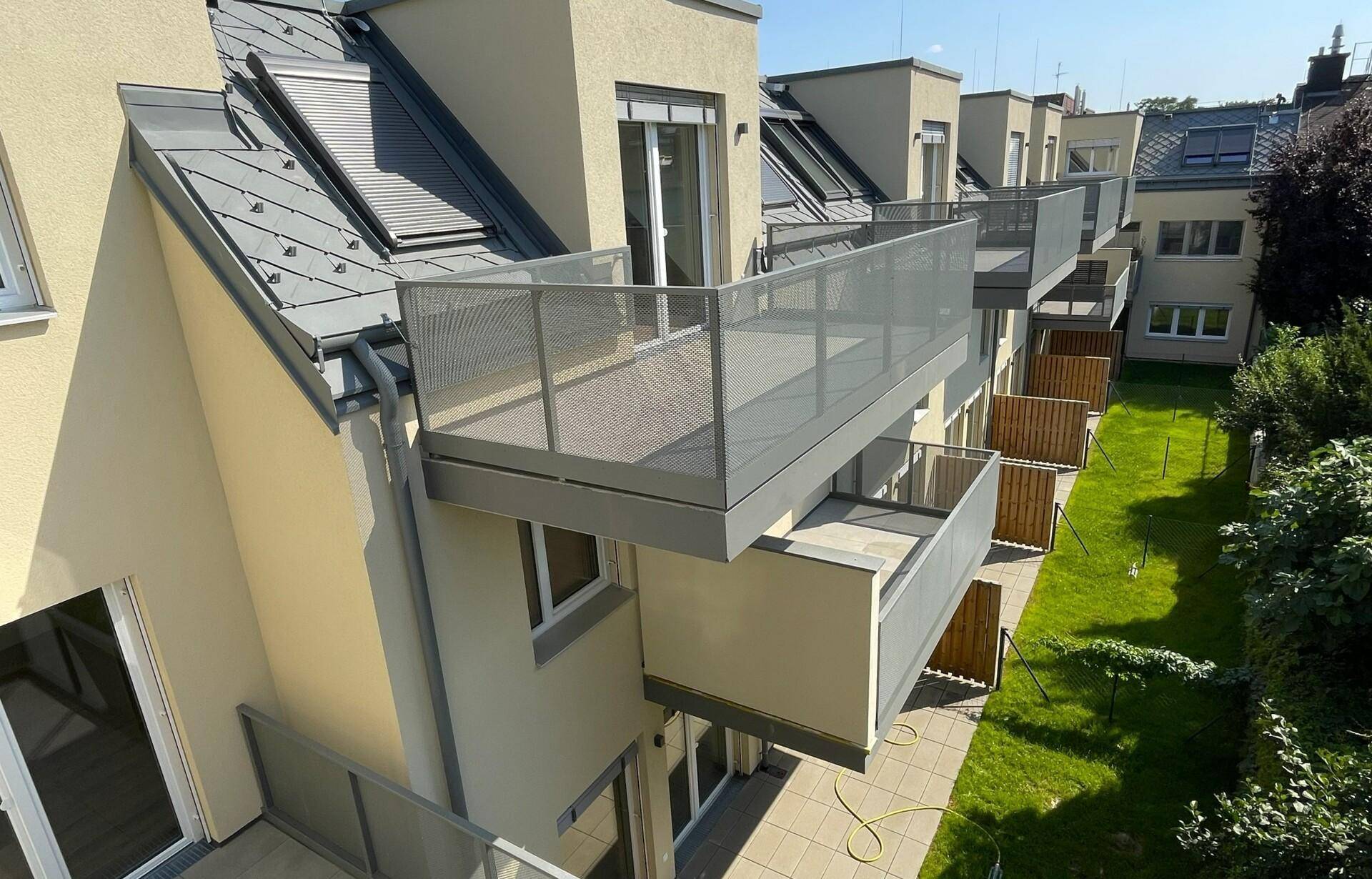 Rückseite eines modernen Wohngebäudes mit mehreren Balkonen und Dachfenstern.