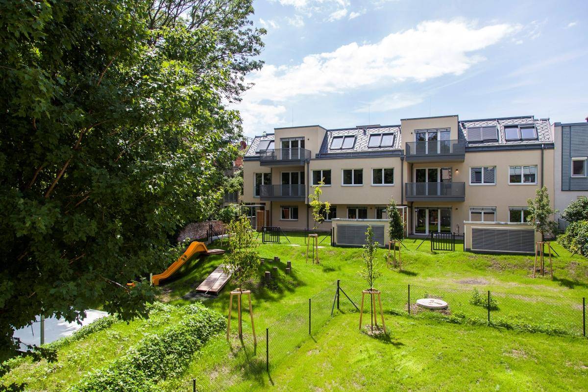 Weitläufige Grünfläche mit Spielplatz und Rutsche hinter einem modernen Wohnkomplex.
