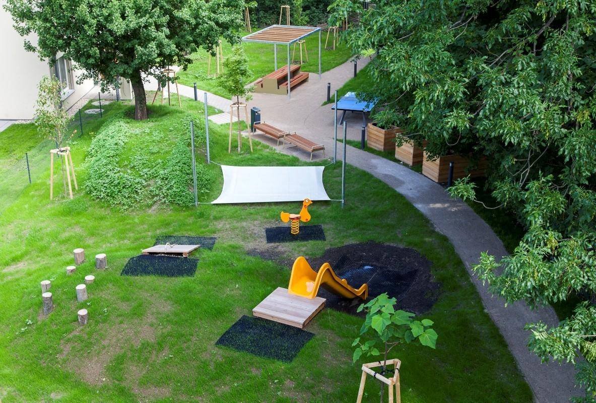 Vogelperspektive auf einen modernen Spielplatz mit Rutsche, Schaukel und Sitzbereichen.
