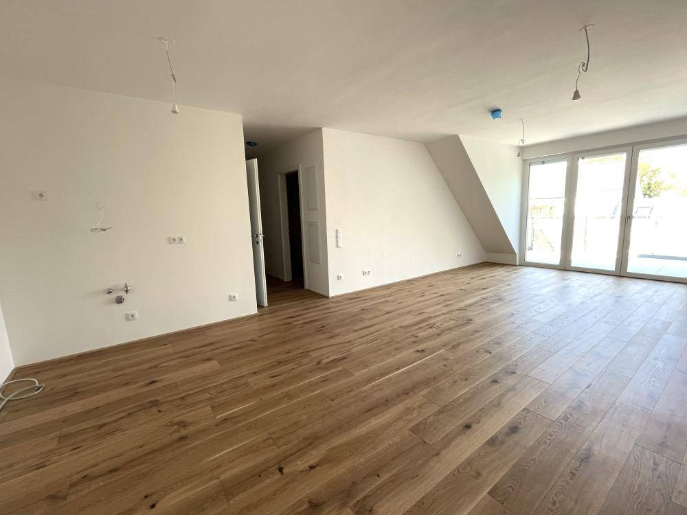 Geräumiger, unmöblierter Wohnbereich mit neuem Holzboden und direktem Zugang zur Terrasse.