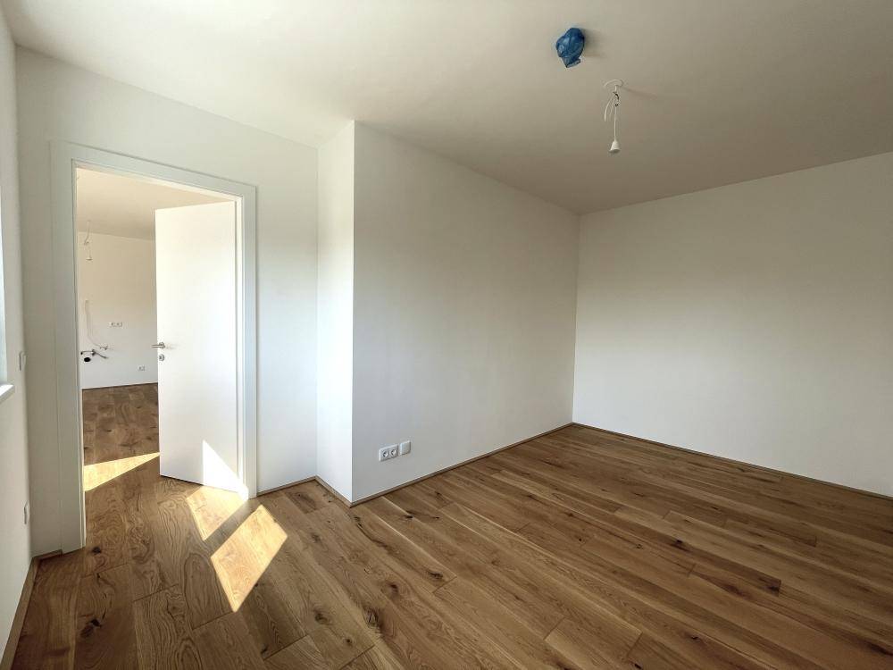 Leeres Zimmer mit hellem Holzboden und weißen Wänden, bereit zur individuellen Gestaltung.