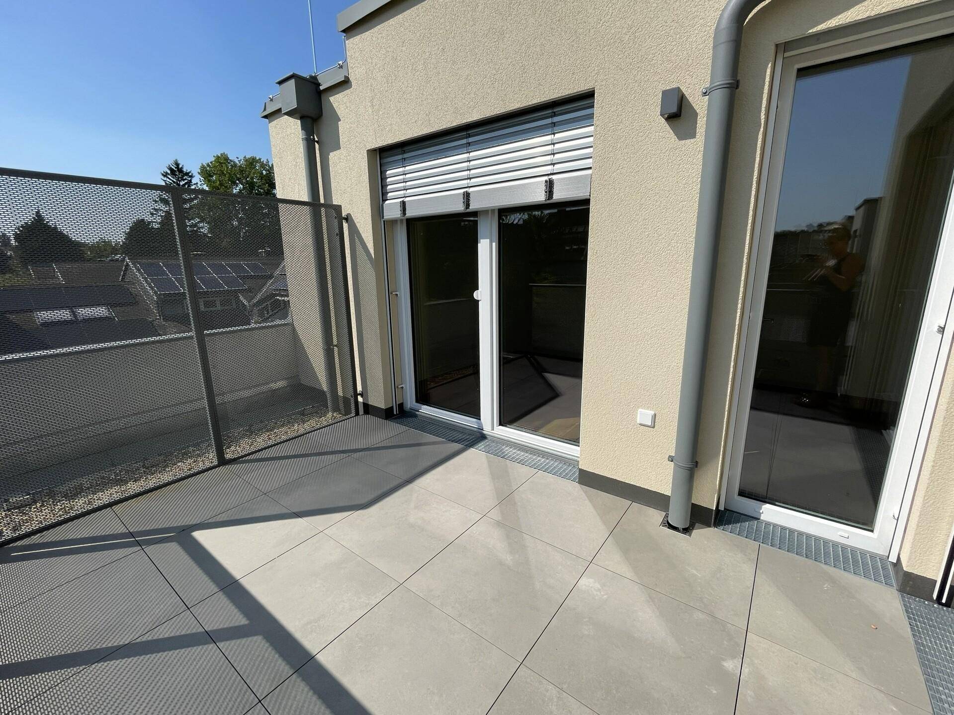 Heller Terrassenbereich mit Fliesenboden und Zugang zu den Innenräumen durch große Glastüren.