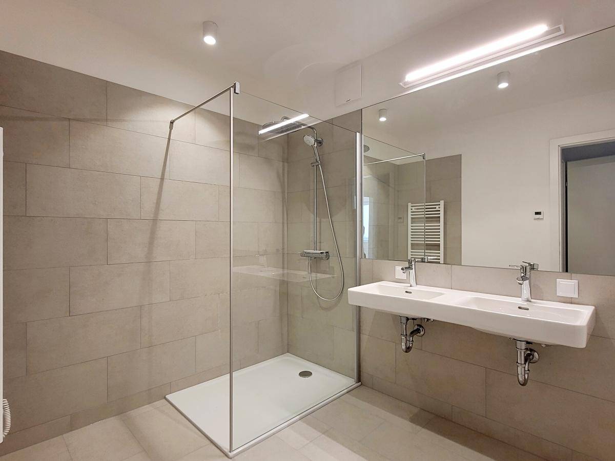 Modernes Badezimmer mit großformatigen Fliesen, Doppelwaschbecken und begehbarer Dusche.