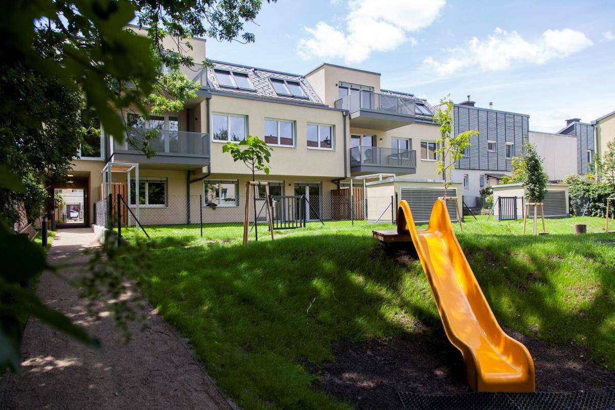 Gemeinschaftsgarten mit Spielplatzrutsche und Blick auf die moderne Wohnanlage.