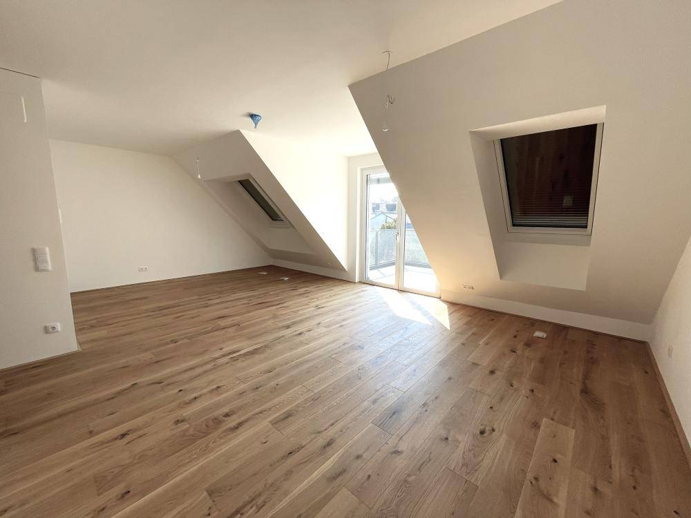 Helles Wohnzimmer im Dachgeschoss mit Holzboden, Dachschrägen und Zugang zu einem Balkon.
