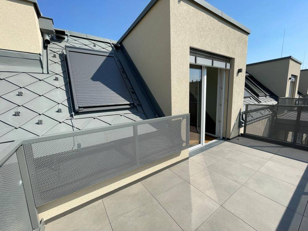 Sonniger Terrassenbereich im Dachgeschoss mit modernem Geländer und Blick auf die Umgebung.