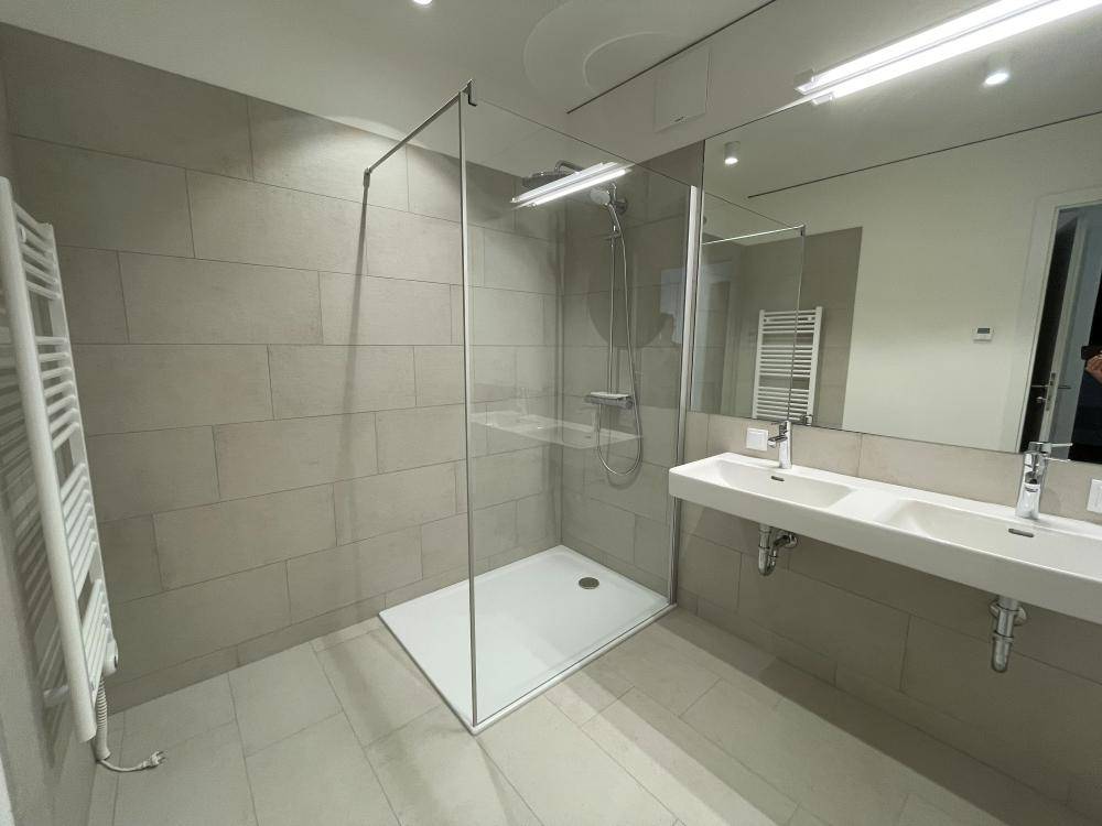 Modernes Badezimmer mit Doppelwaschbecken, großer begehbarer Dusche und beheiztem Handtuchhalter.