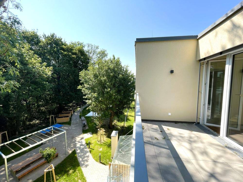 Balkon mit weitem Blick über die grüne Gemeinschaftsfläche und die umliegenden Bäume.