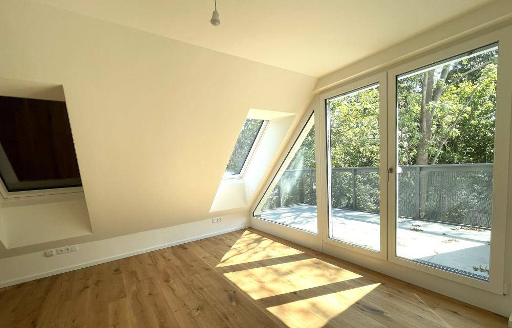 Helles Zimmer im Dachgeschoss mit Holzboden, großen Fenstern, Dachfenster und Balkonzugang.