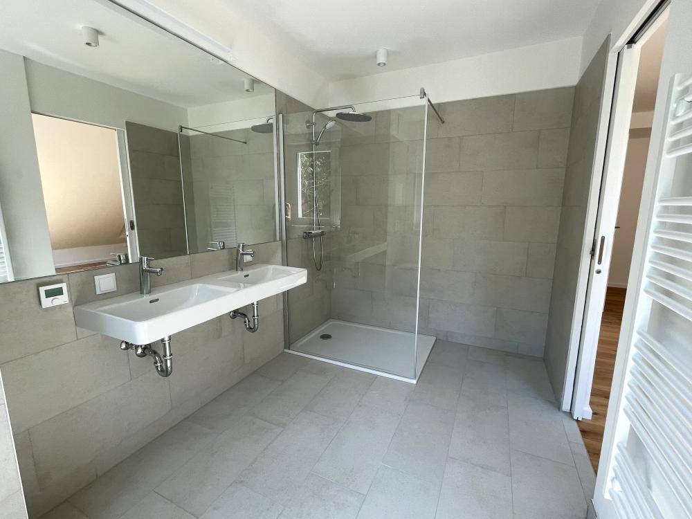 Modernes Badezimmer mit großformatigen grauen Fliesen, Doppelwaschbecken und begehbarer Dusche.