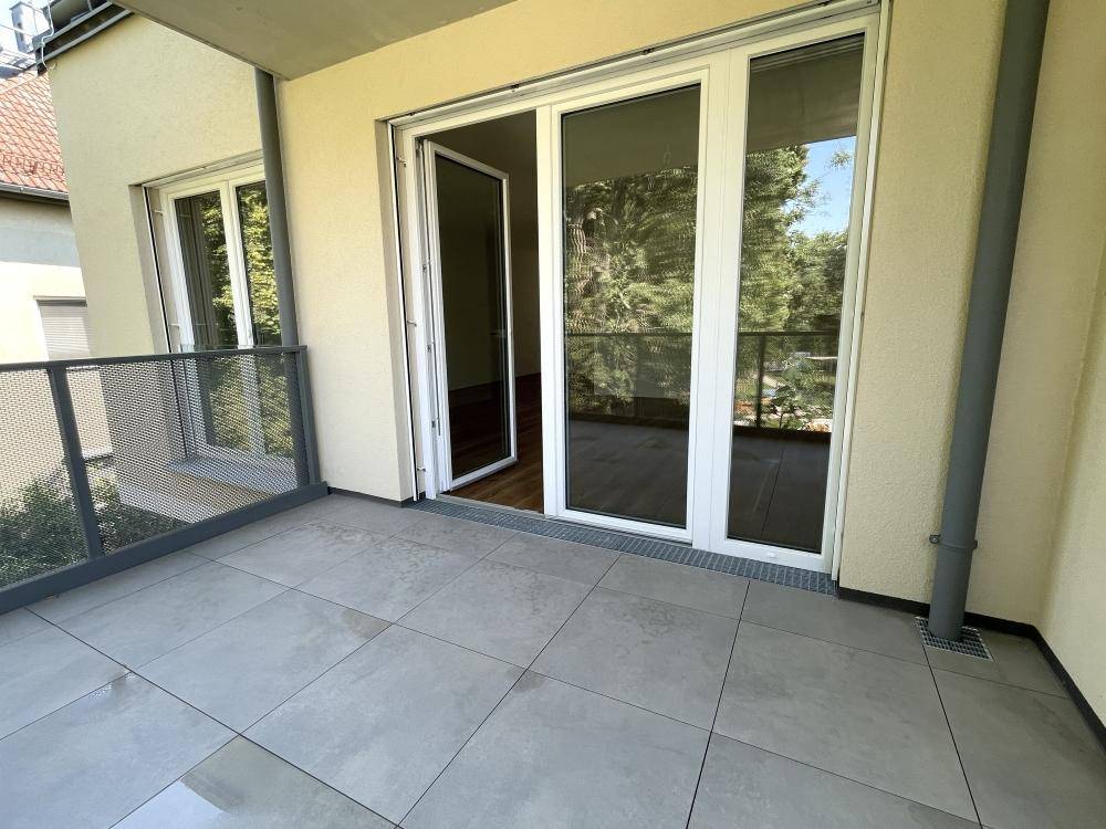Moderner Balkon mit Fliesenboden und Zugang zu einem hellen Innenraum durch große Glastüren.