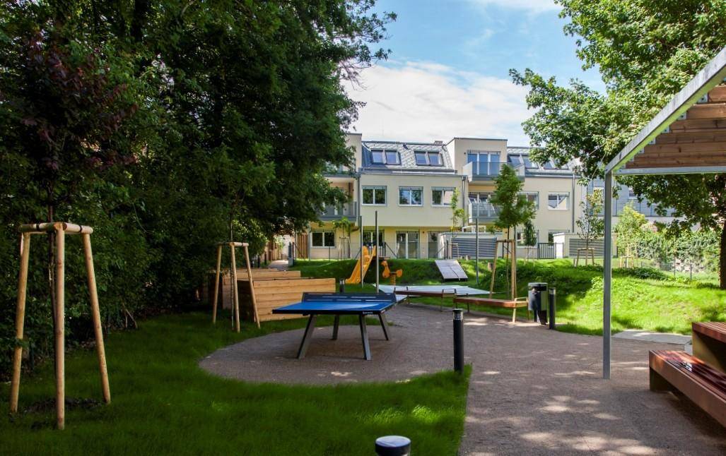 Gemeinschaftsgarten mit Spielplatz, Tischtennistisch und Blick auf die moderne Wohnanlage.