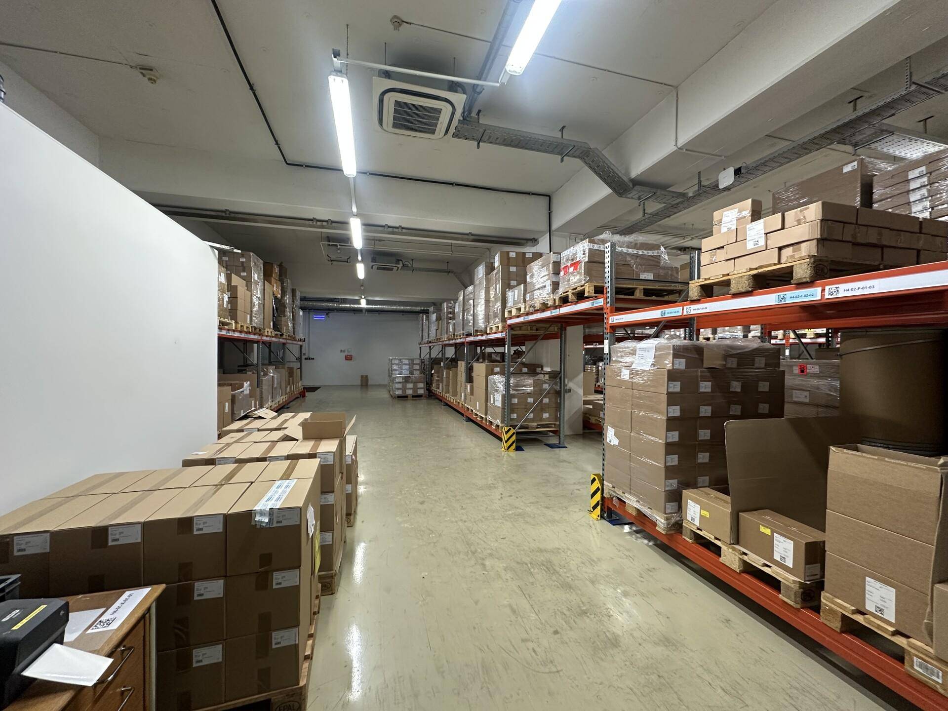 Langer Gang in einem Lagerraum mit hohen Regalen voller Kartons und industrieller Beleuchtung.