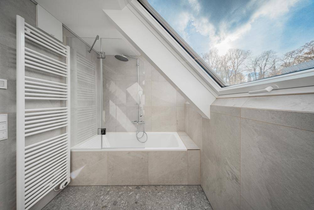 Helles Badezimmer mit Badewanne, Dusche, beheiztem Handtuchhalter und großem Dachfenster.