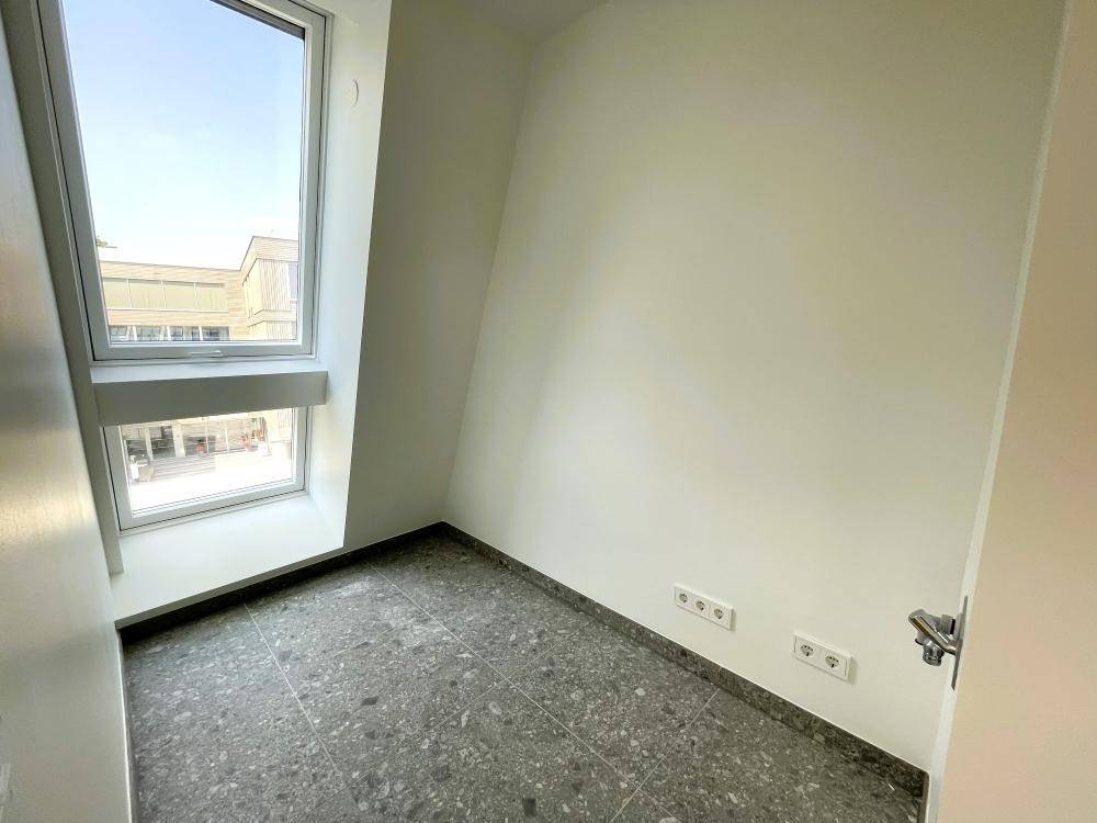 Kleiner Raum mit grauem Fliesenboden und Fenster, ideal als Abstellraum oder Garderobe.