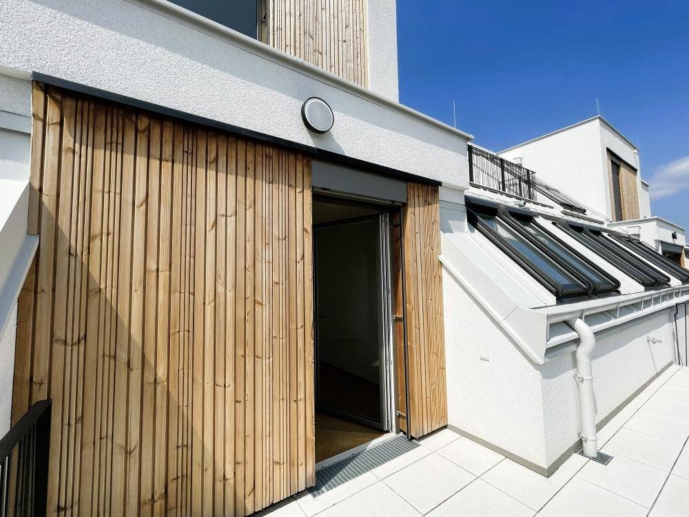 Moderne Gebäudefassade mit Holzverkleidung, weißen Wänden und Dachfenstern.
