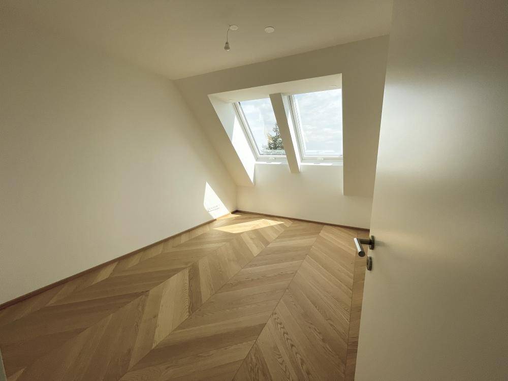 Helles Schlafzimmer mit Fischgrätparkett und schrägen Dachfenstern für viel Tageslicht.