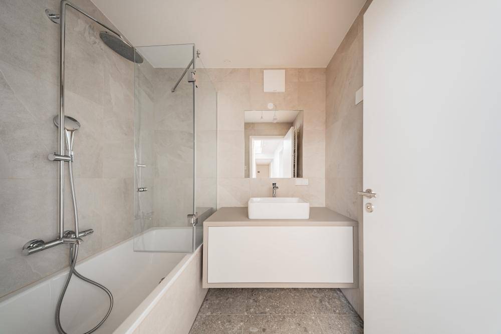 Helles Badezimmer mit Badewanne, Duschfunktion, modernem Waschtisch und hellen Fliesen.