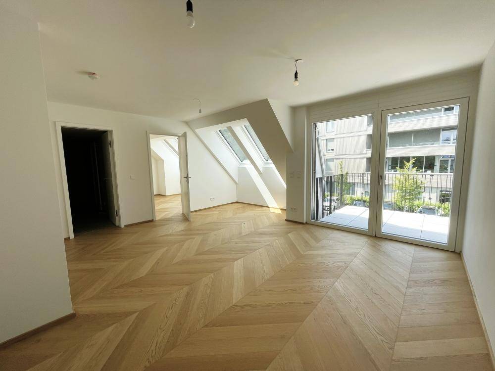 Lichtdurchfluteter Wohnraum mit elegantem Fischgrätparkett, großen Fenstern und direktem Balkonzugang.