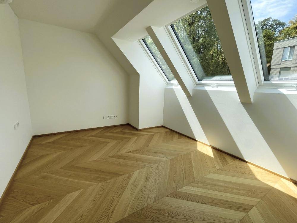 Helles Zimmer mit schrägem Dach, Fischgrätparkett und großen Dachfenstern für viel natürliches Licht.