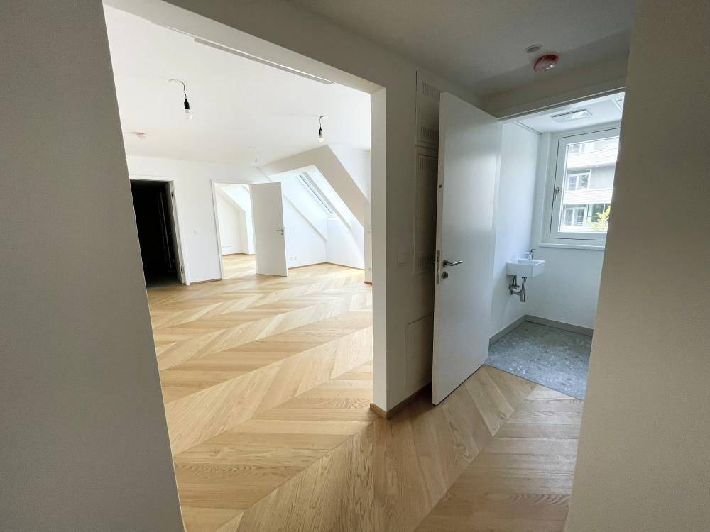 Heller Flur mit elegantem Fischgrätparkett, der zu verschiedenen leeren Räumen und einem Gäste-WC führt.