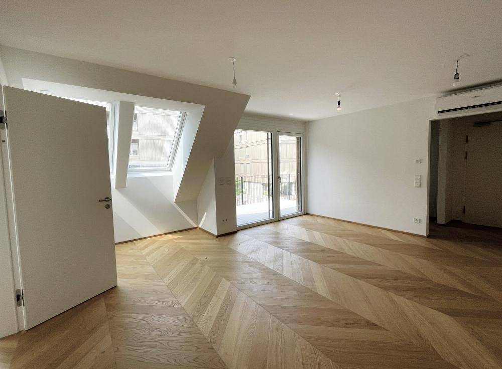 Geräumiger, heller Wohnbereich mit Fischgrätparkett, Dachfenstern und Zugang zu einem sonnigen Balkon.