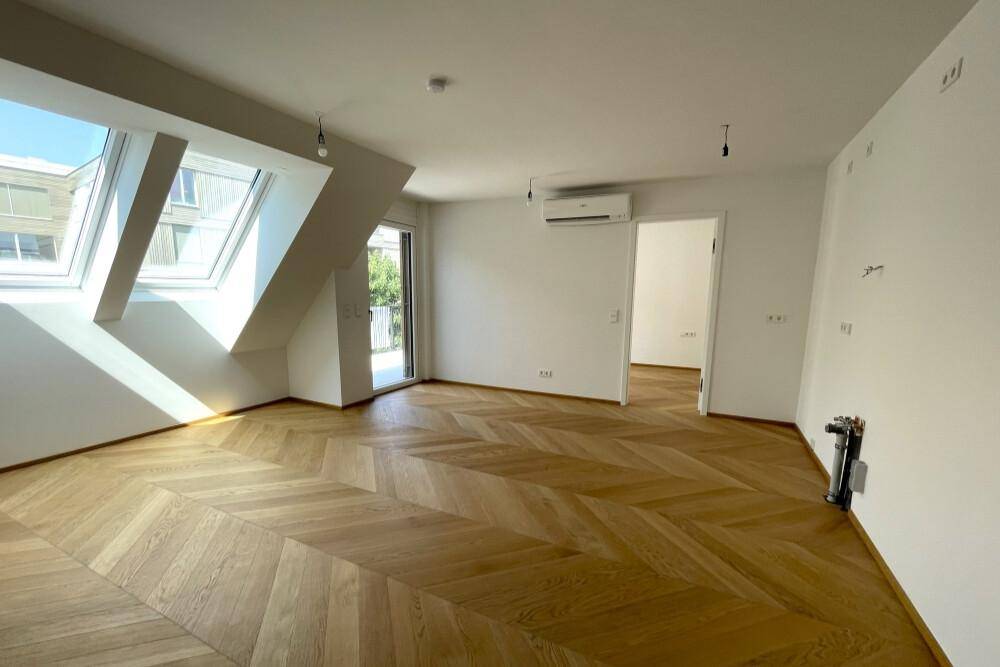 Heller Wohnraum mit Fischgrätparkett, Dachfenstern und Zugang zum Balkon.