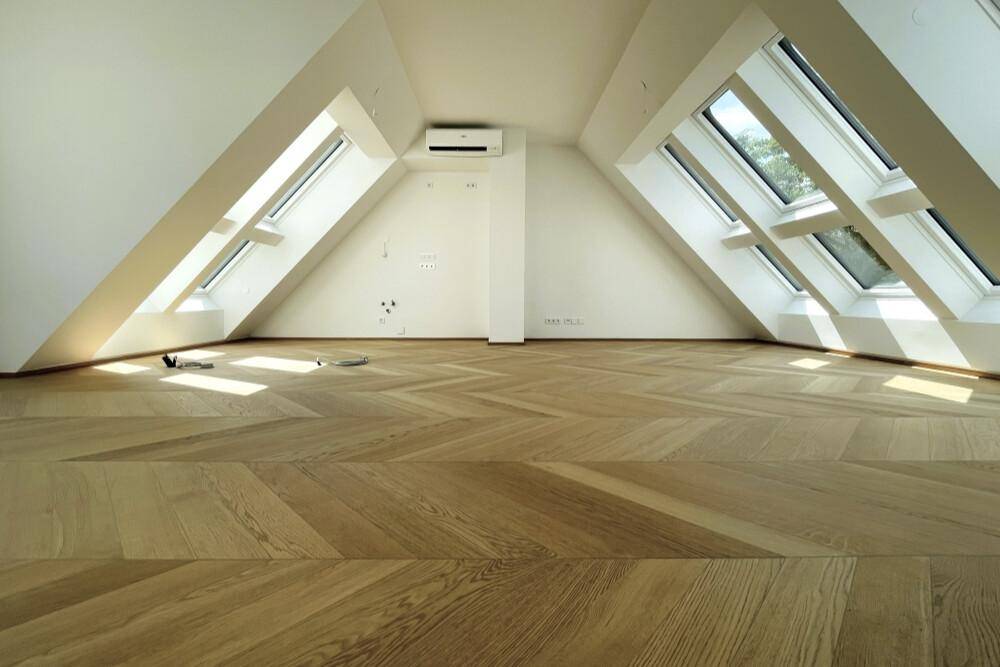 Heller Raum mit elegantem Fischgrätparkett, Dachschrägen und integrierter Klimaanlage.