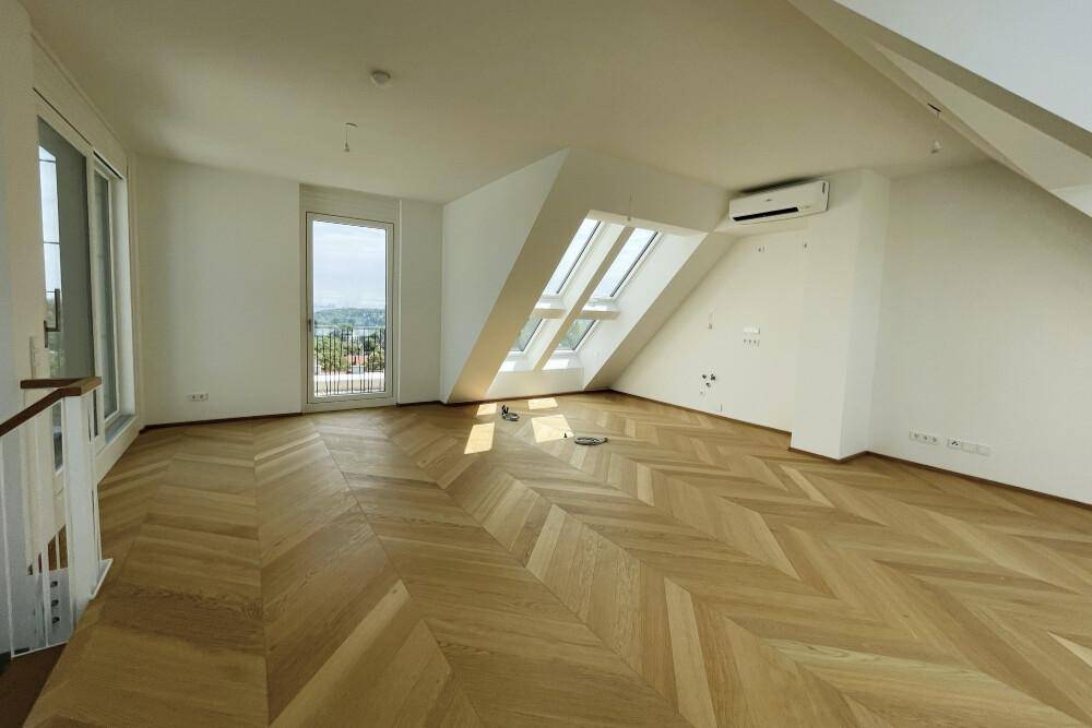 Lichtdurchfluteter Wohnbereich mit Fischgrätparkett, Dachschrägen und Zugang zu einem Balkon.
