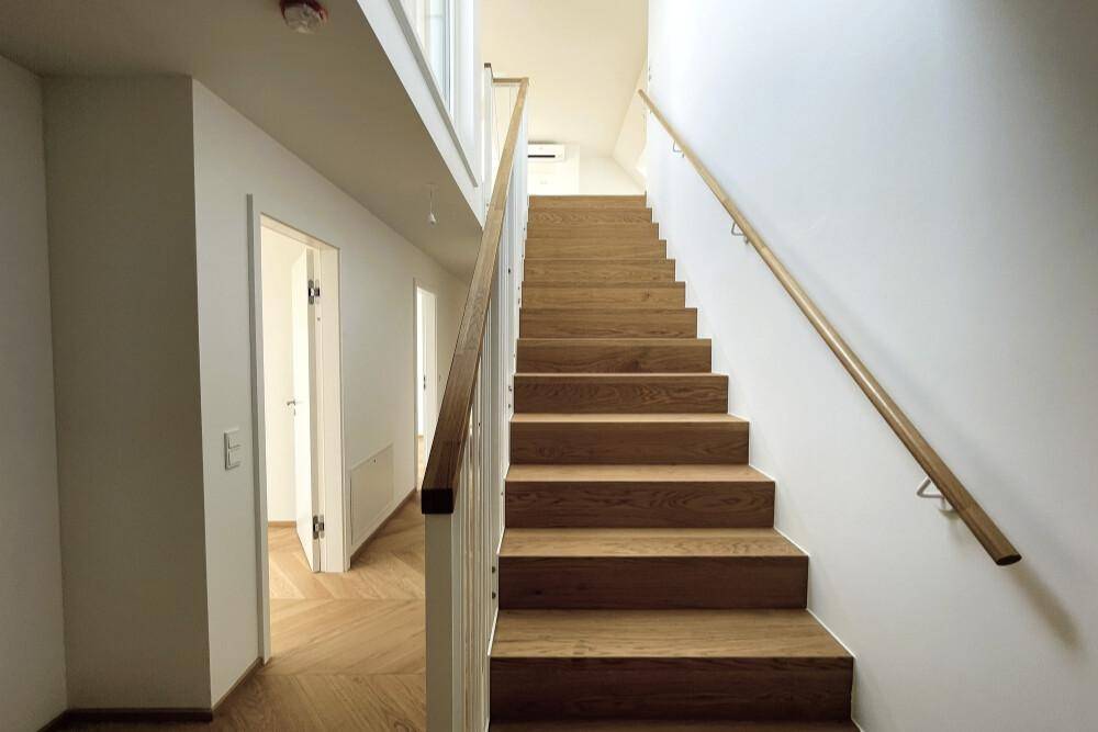 Moderner Treppenaufgang mit Holzstufen und hellem Geländer, verbindet die Ebenen der Wohnung.