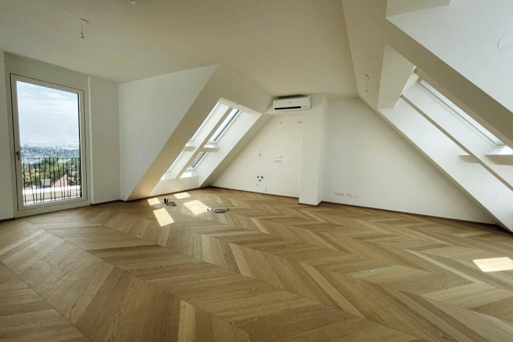 Großer, heller Raum mit Fischgrätparkett, Dachschrägen und weitem Blick durch die Fenster.
