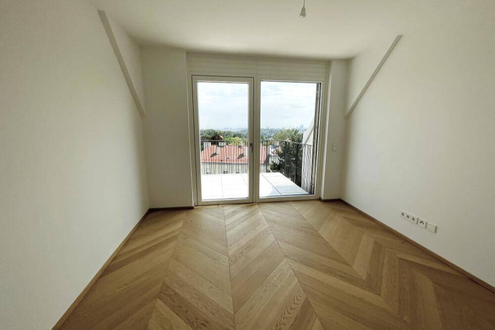 Helles Zimmer mit Fischgrätparkett und großem Fenster mit Blick auf die Umgebung.