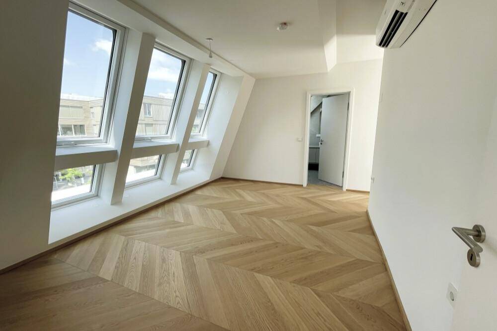 Helles Zimmer mit Fischgrätparkett, Dachschrägen und mehreren Dachfenstern für viel Tageslicht.