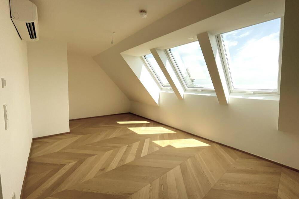 Helles Zimmer mit Fischgrätparkett, Dachschrägen und mehreren Dachfenstern für viel Tageslicht.