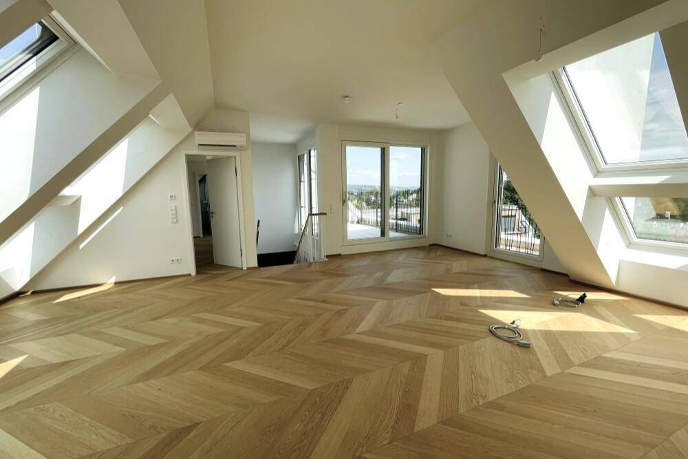 Lichtdurchfluteter Wohnbereich mit modernem Fischgrätparkett und Zugang zu einem Balkon.