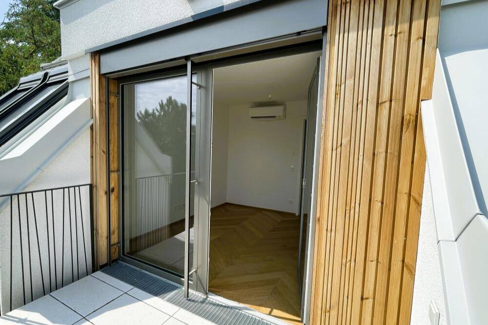 Zugang zum Balkon von einem hellen Zimmer mit Holzverkleidung und Klimaanlage.