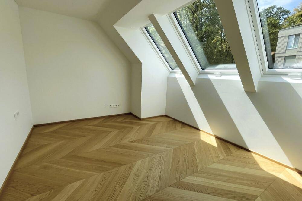Sonniges Zimmer mit schrägen Dachfenstern, Fischgrätparkett und viel natürlichem Lichteinfall.