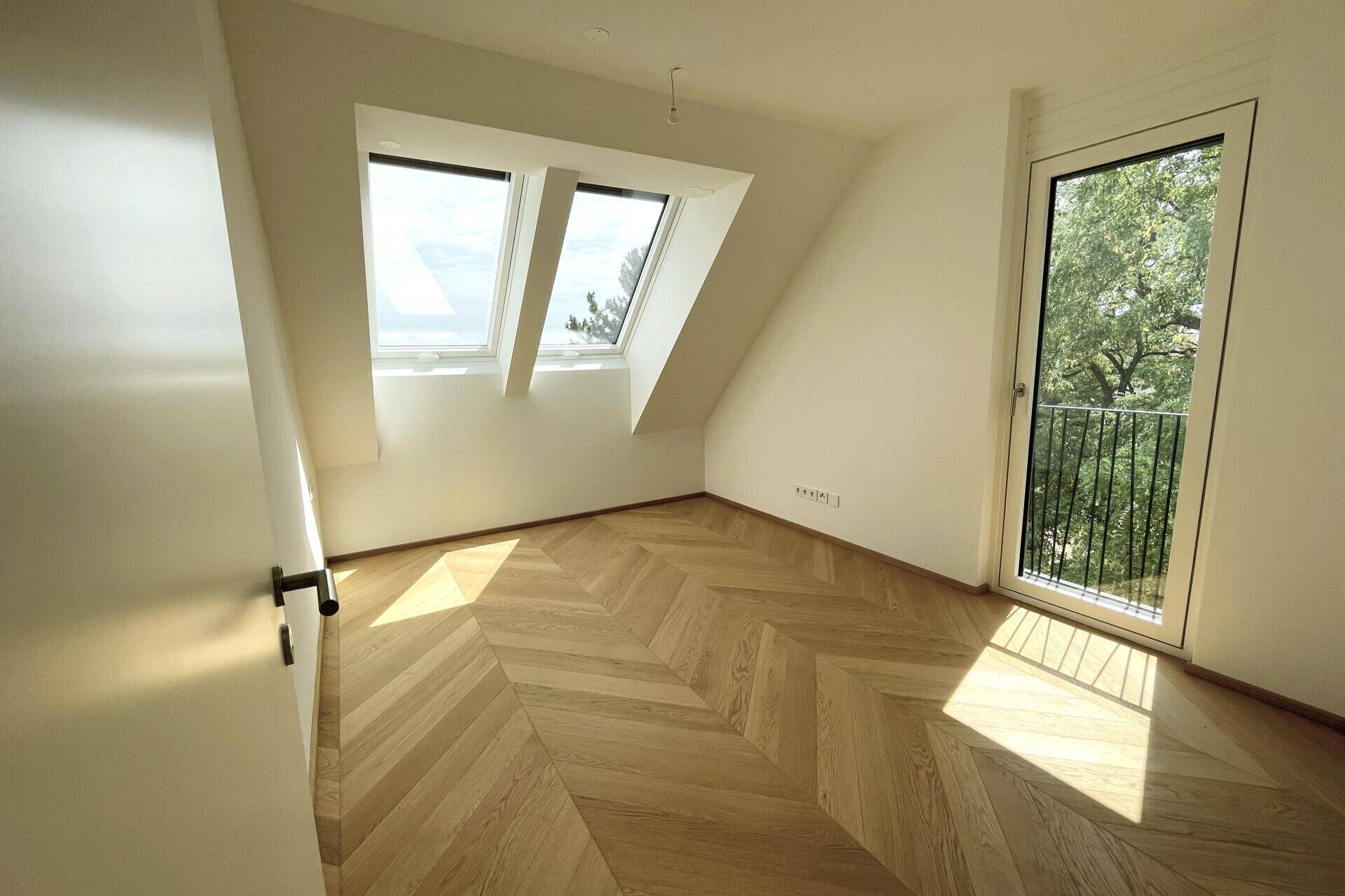 Geräumiges Zimmer mit Fischgrätparkett, Dachschrägen und Zugang zu einem französischen Balkon.