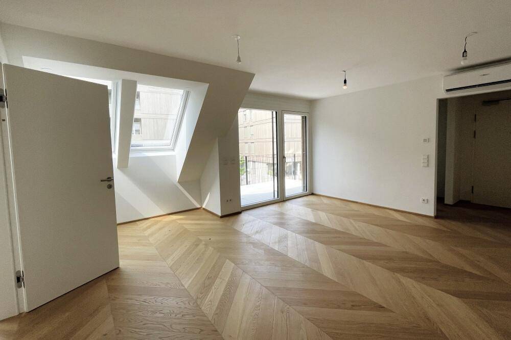 Lichtdurchfluteter Wohnbereich mit Fischgrätparkett, Dachschrägen und Zugang zu einem sonnigen Balkon.