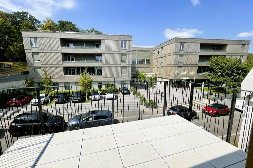Blick vom Balkon auf die moderne Wohnanlage mit Parkplätzen und umliegender Grünfläche.