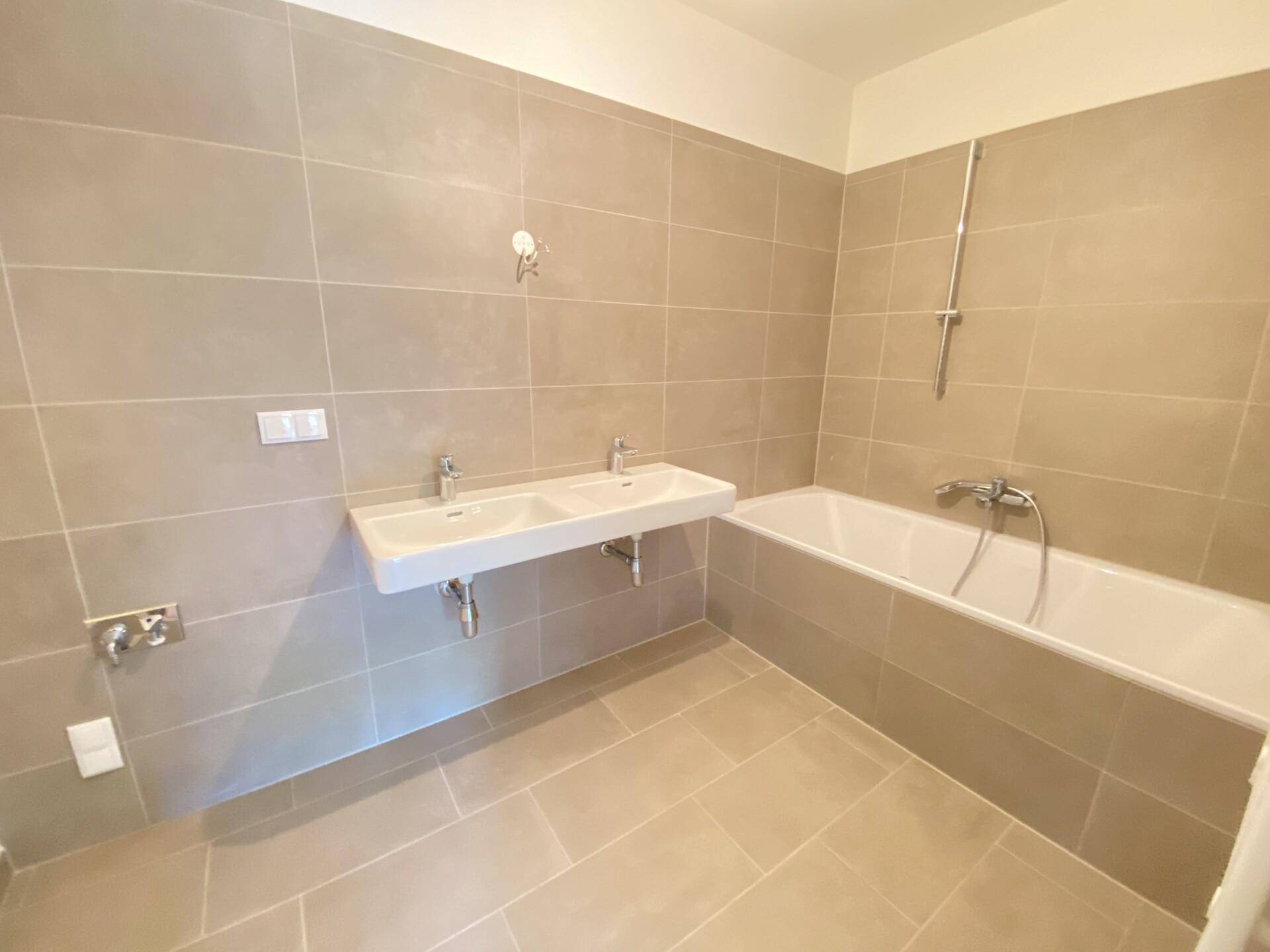 Gefliestes Badezimmer mit Badewanne und Doppelwaschbecken in neutralen Farbtönen.