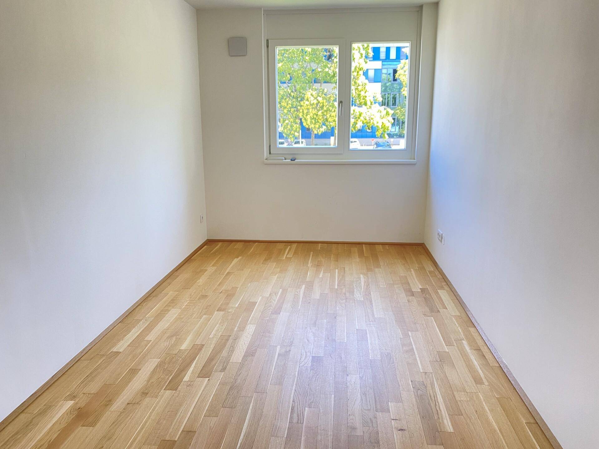 Leeres Zimmer mit Parkettboden und Fenster, geeignet als Schlaf- oder Kinderzimmer.