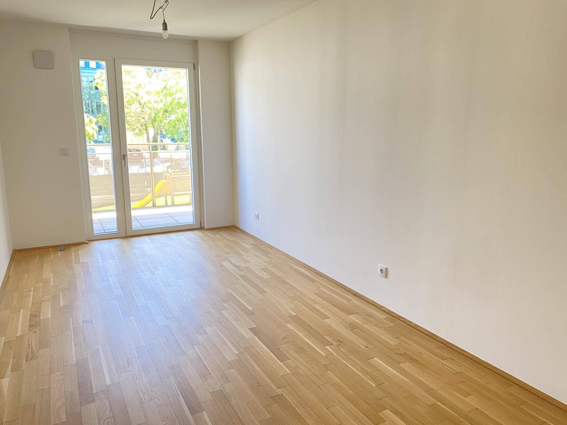 Heller Raum mit Parkettboden und Zugang zu einem Balkon, ideal als Schlafzimmer.
