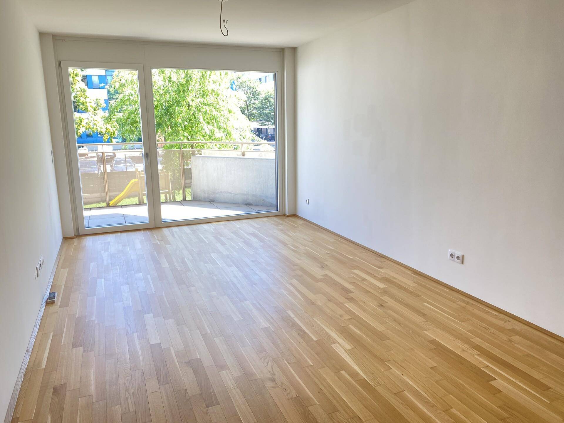 Heller, leerer Raum mit Parkettboden und großen Glastüren zum Balkon.