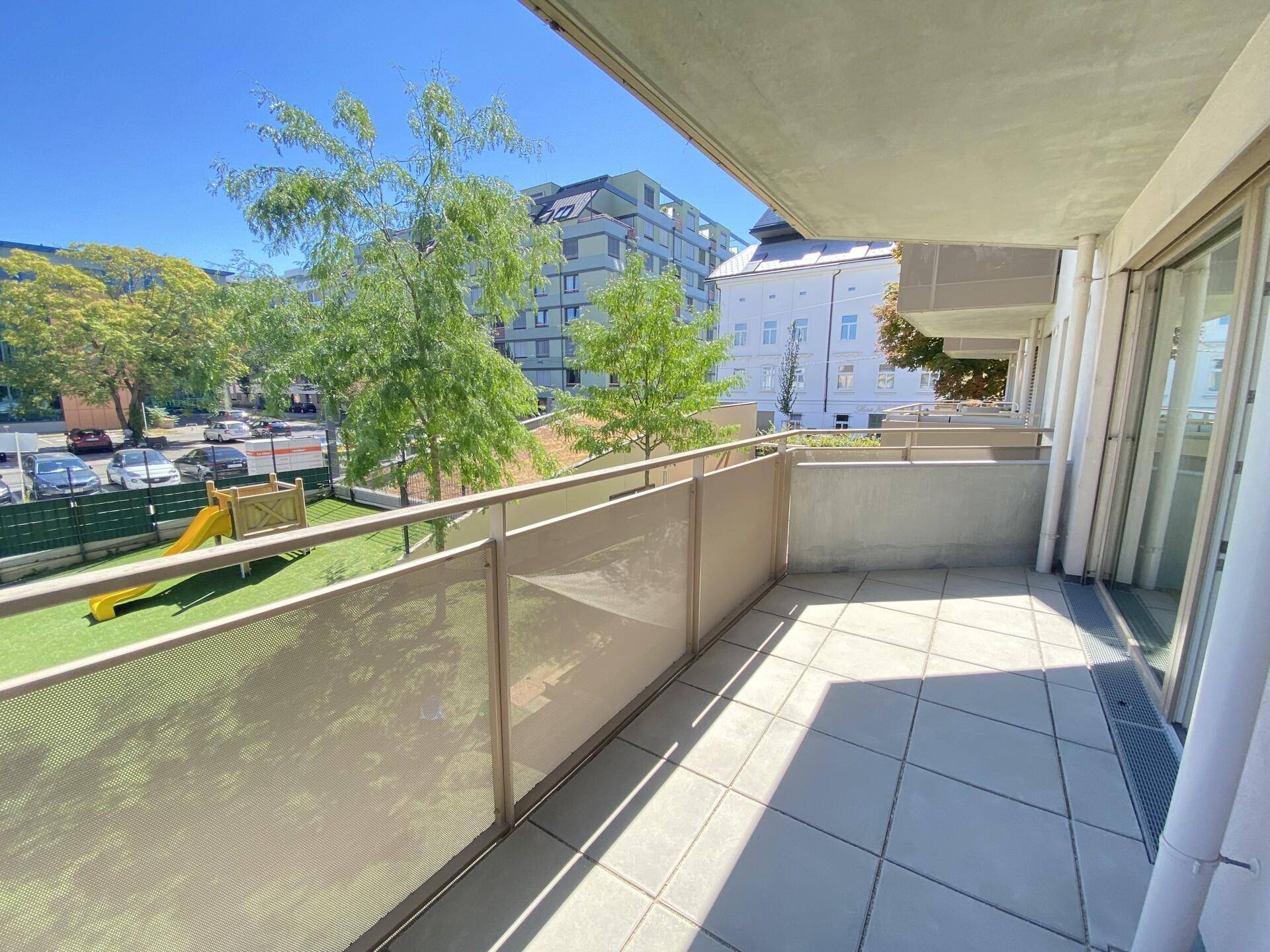 Geräumiger Balkon mit Fliesenboden und Blick auf einen Spielplatz und die Umgebung.