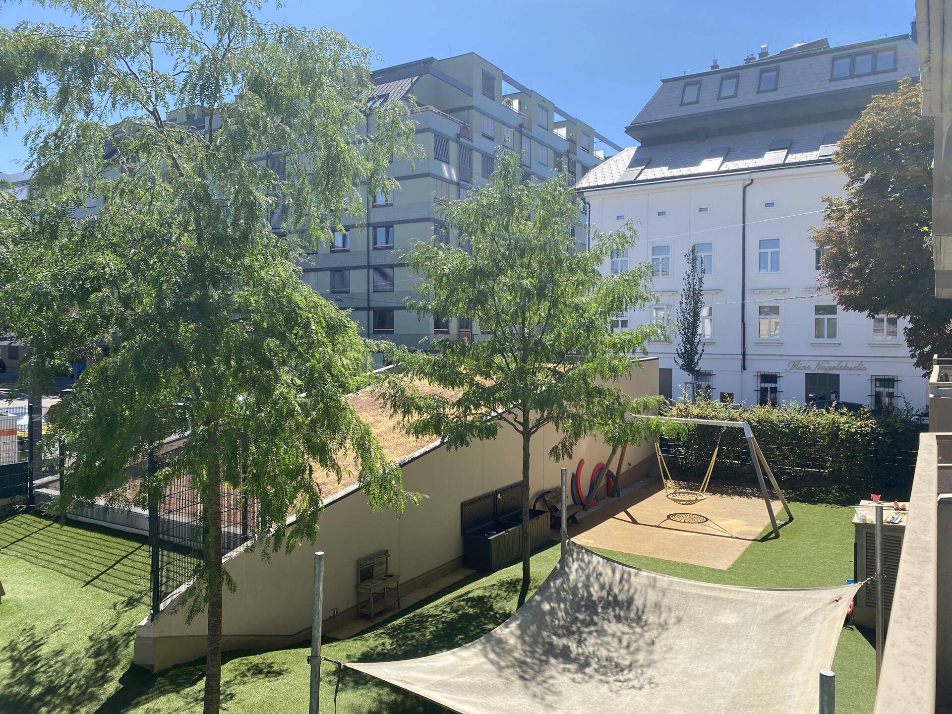 Blick auf einen Spielplatz mit Schaukeln und einem begrünten Dach in der Wohnanlage.